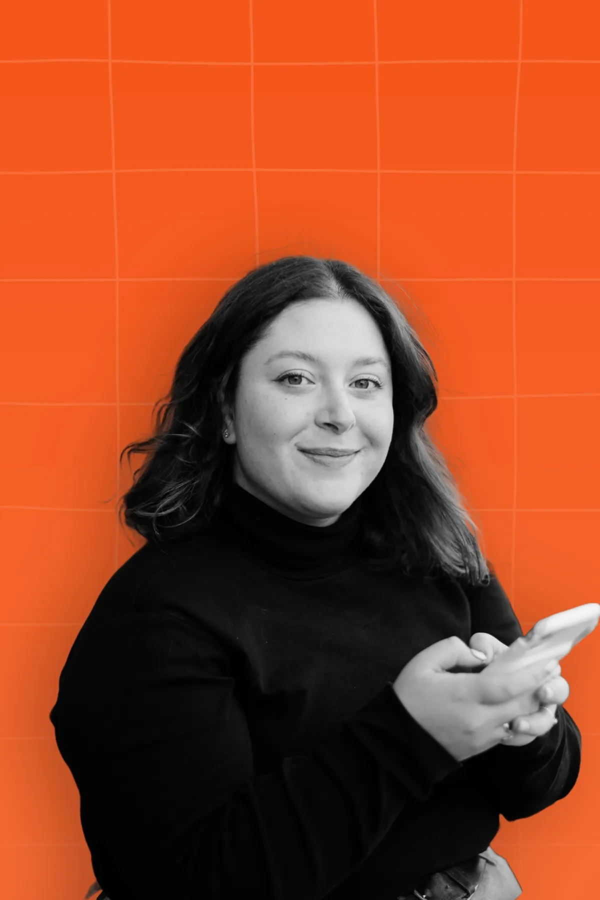 Black and white portrait of a woman smiling and holding phone placed on orange background with light orange pattern.